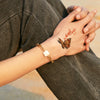 A hand wearing a gold bracelet and featuring a butterfly temporary body art sticker on the wrist against dark clothing.