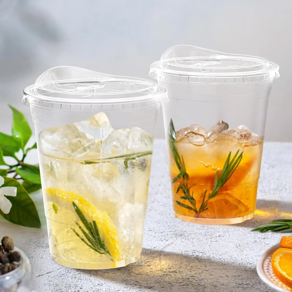 Two clear plastic cups filled with iced tea and garnished with citrus slices and rosemary.