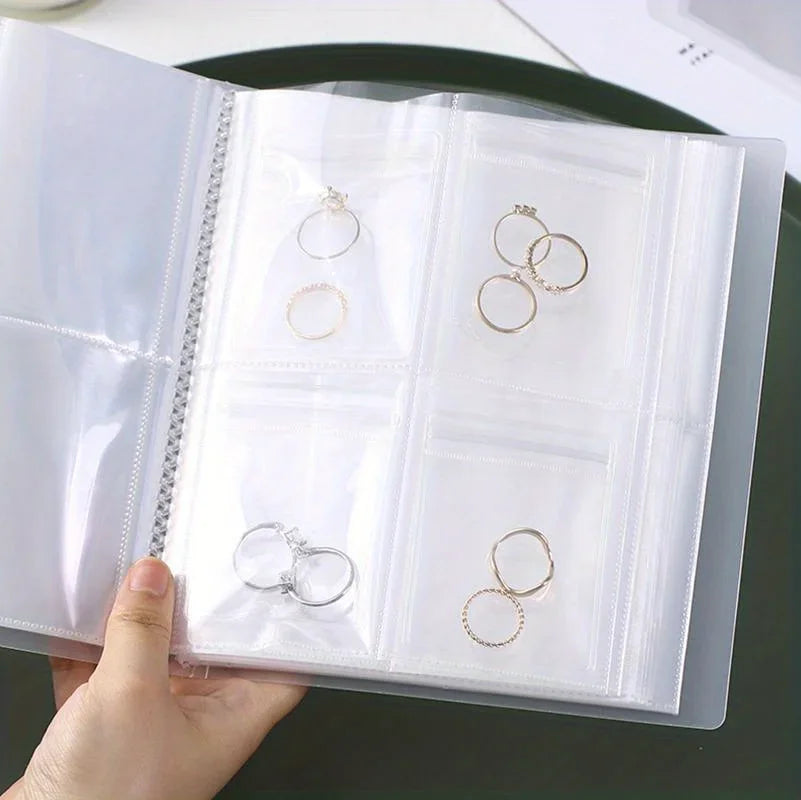 A transparent jewelry organizer storage bag displaying various rings and jewelry pieces in individual plastic grids.
