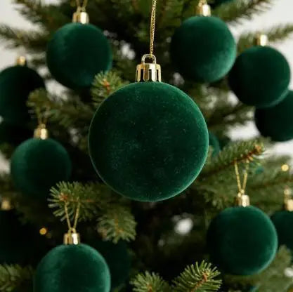 A close-up of five deep emerald green velvet flocked Christmas tree ornaments hanging on a green fir branch.