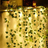 Artificial leaf string lights draped across a fabric background creating a glowing green vine effect