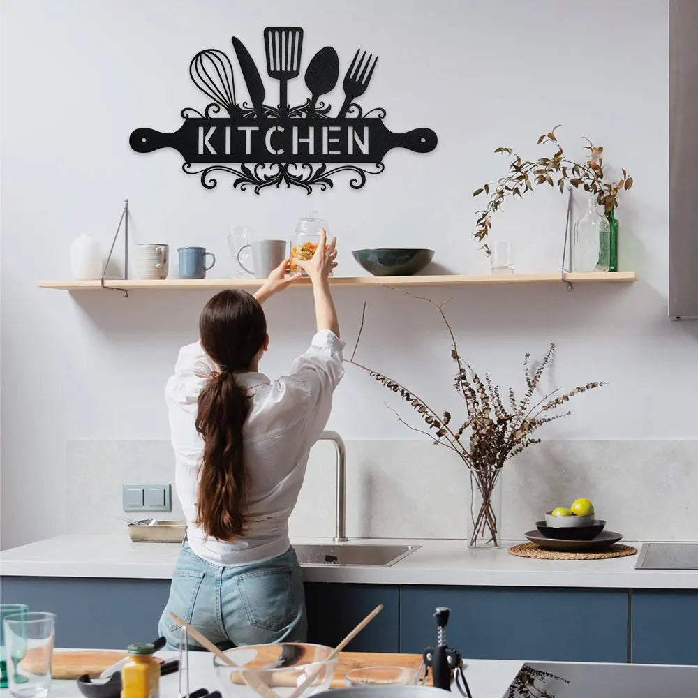 A woman in a white shirt is placing a metal kitchen sign on a wooden shelf above a sink area.
