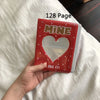 A hand holds a red photo album titled Mine with a heart design, resting on white bedding.