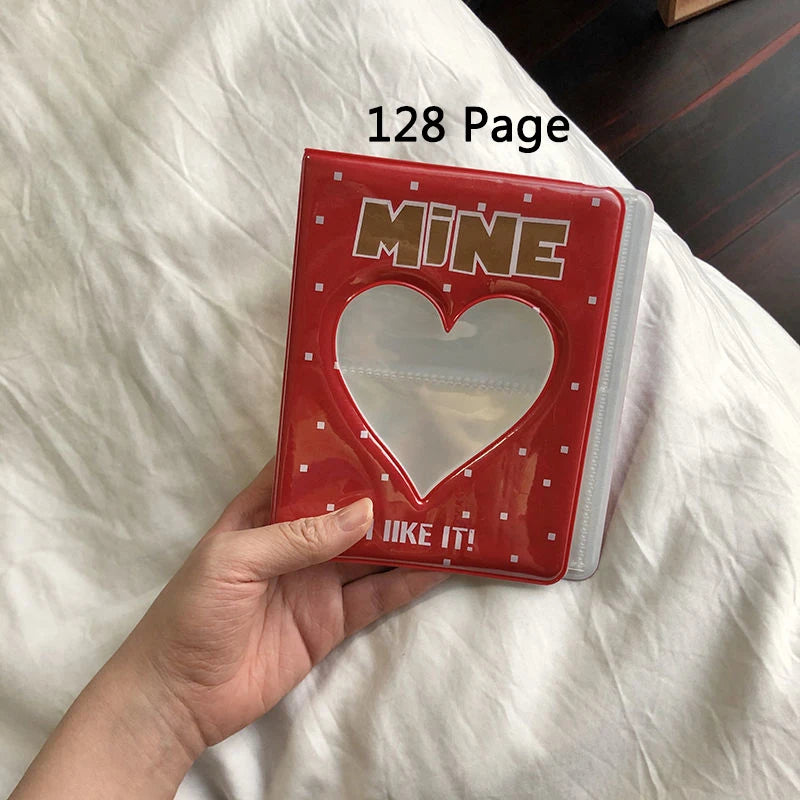 A hand holds a red photo album titled Mine with a heart design, resting on white bedding.