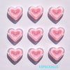 Six pink heart-shaped acrylic charms casting shadows on a white surface.