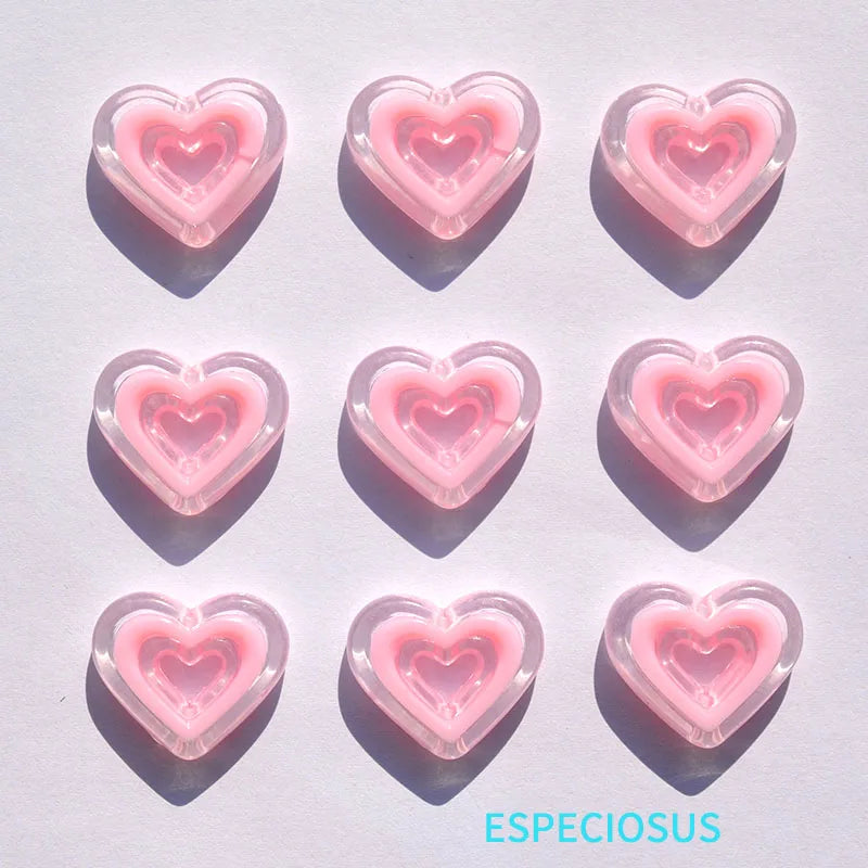 Six pink heart-shaped acrylic charms casting shadows on a white surface.