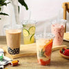 Three colorful iced beverages in clear plastic cups with straws are displayed on a wooden board.