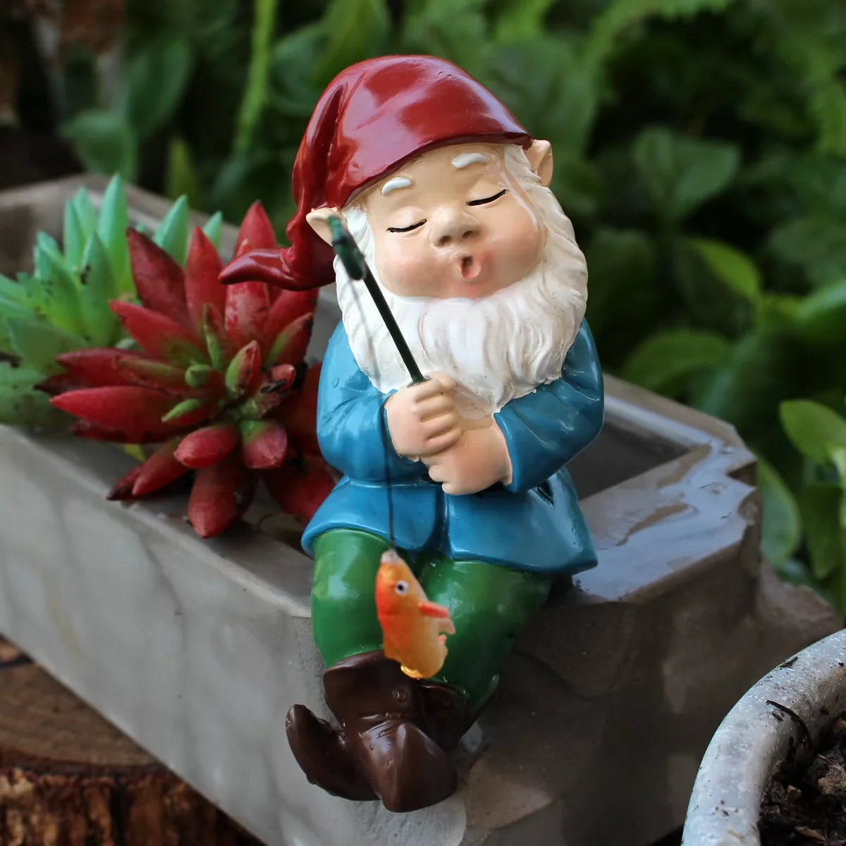 Dekorative Angelfigur mit rotem Hut und weißem Bart auf einem Steintopf.