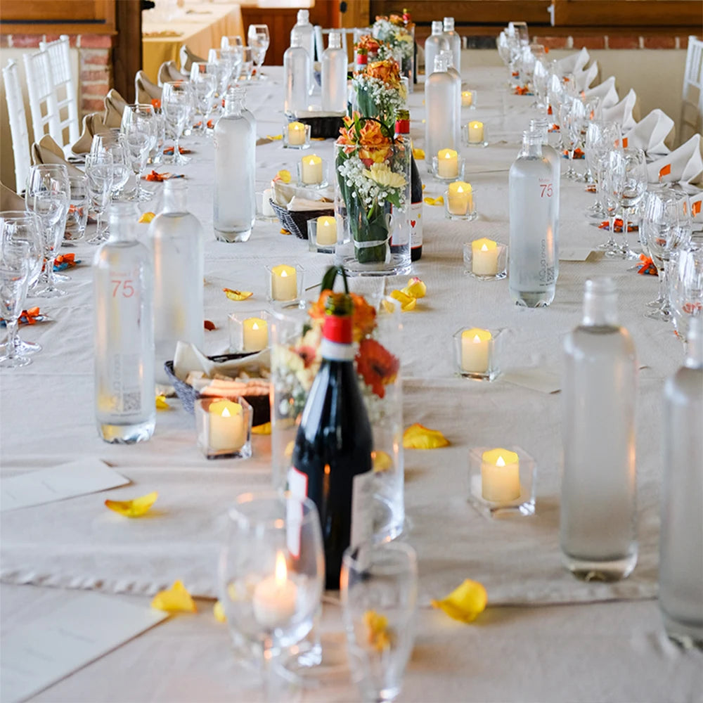 A long table setting featuring clear glass bottles and LED tea light candles for an event.