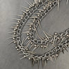 A close-up of a heavy punk rivet biker style chain necklace made of silver metal spikes.