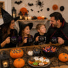 A family of three laughing around a table with Halloween witch cauldrons and pumpkins.