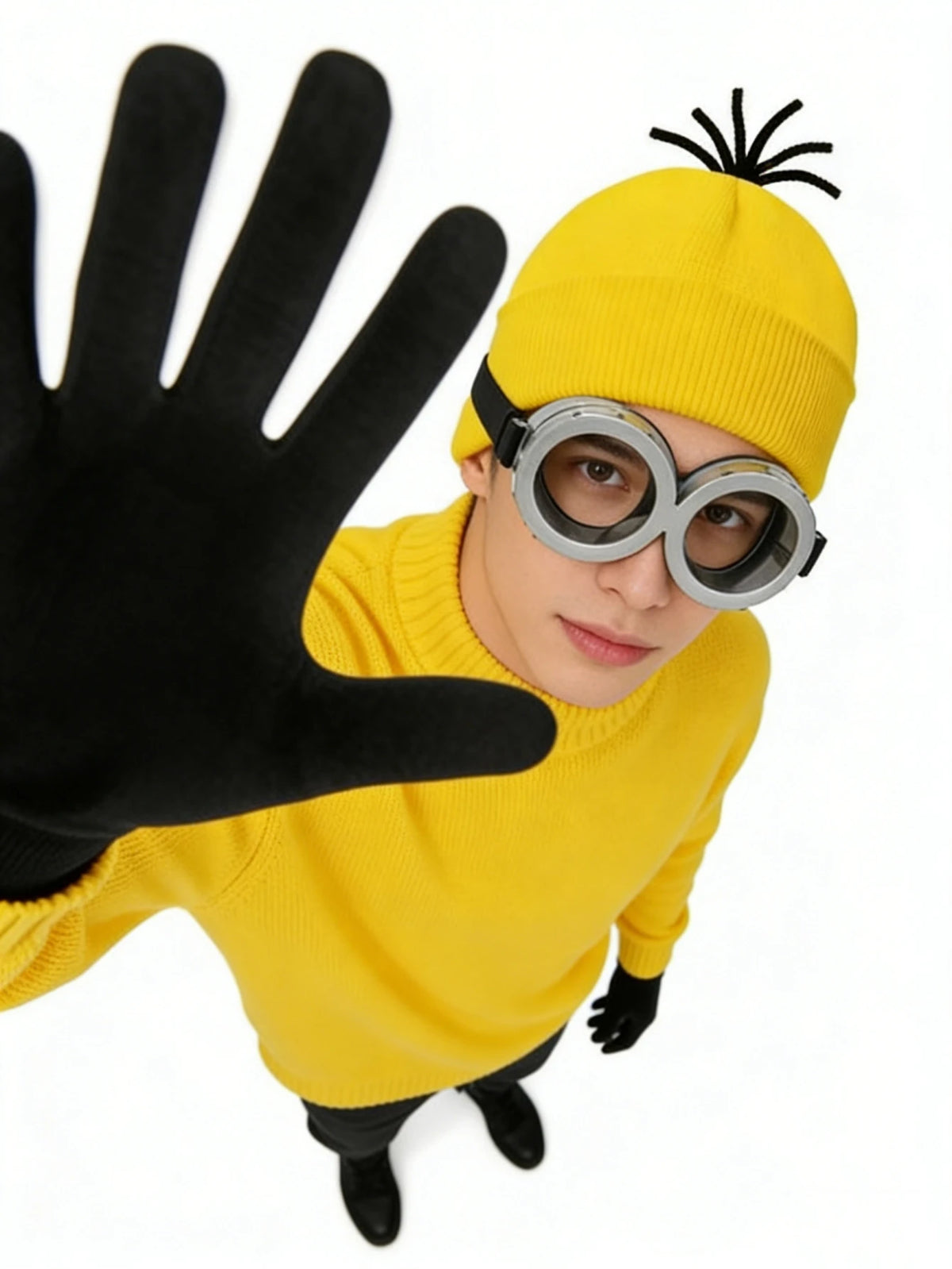 A person wearing a yellow knitted hat, black gloves, and silver-rimmed round glasses.