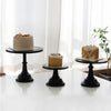 A tiered metal cake stand displaying a light-colored cake with cream frosting on a white table.