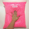 A hand is holding a clear bag filled with pink foam beads for crafting and decoration.