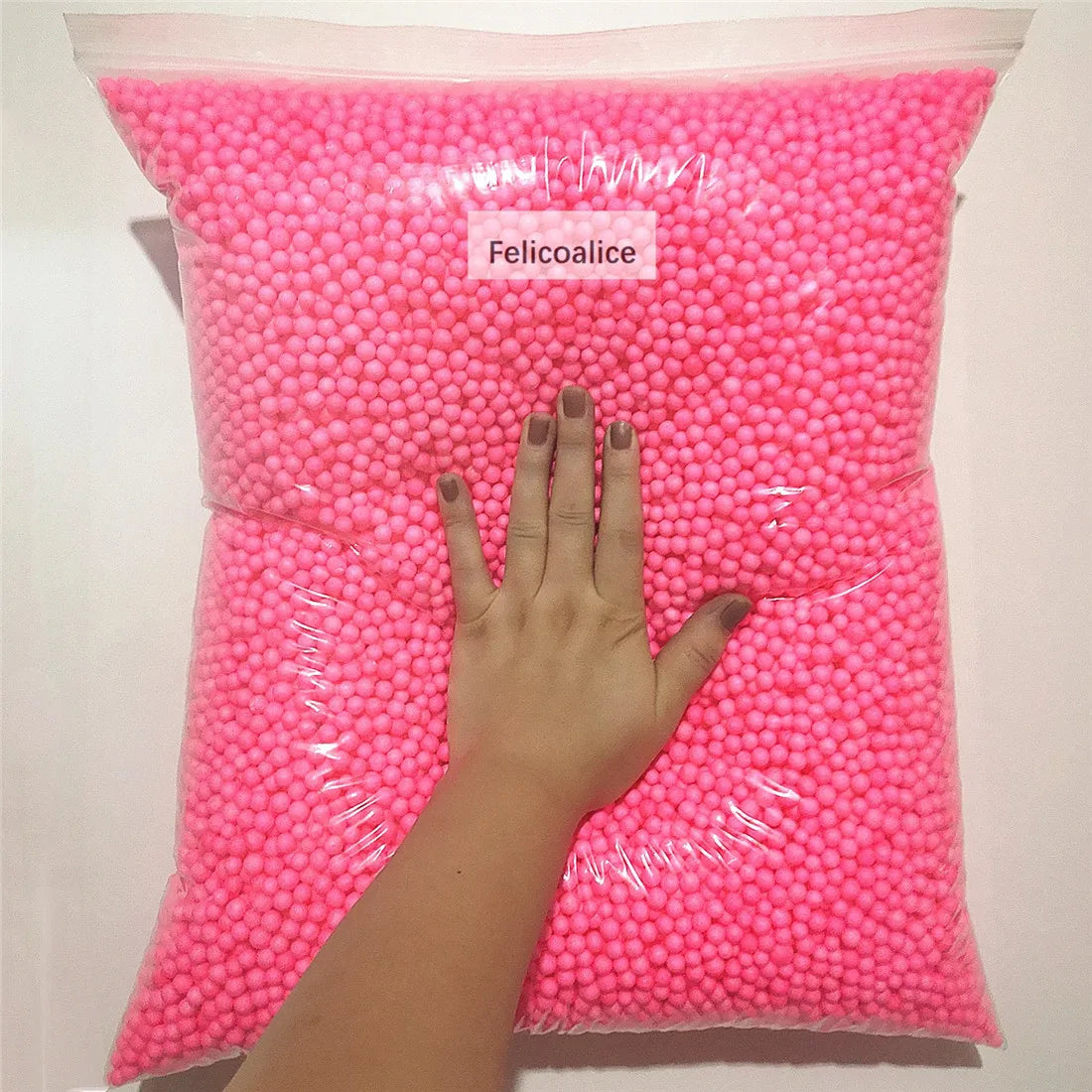 A hand is holding a clear bag filled with pink foam beads for crafting and decoration.