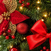 A close-up of a festive Christmas garland featuring red ribbon, gold accents, and sparkling ornaments on green pine branches.