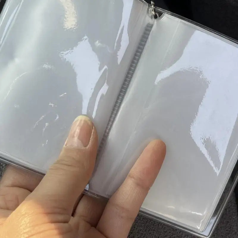 A hand is opening a mini transparent photo album with a clear plastic cover and a silver zipper.
