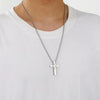 A silver stainless steel cross pendant necklace worn around the neck against a white t-shirt.