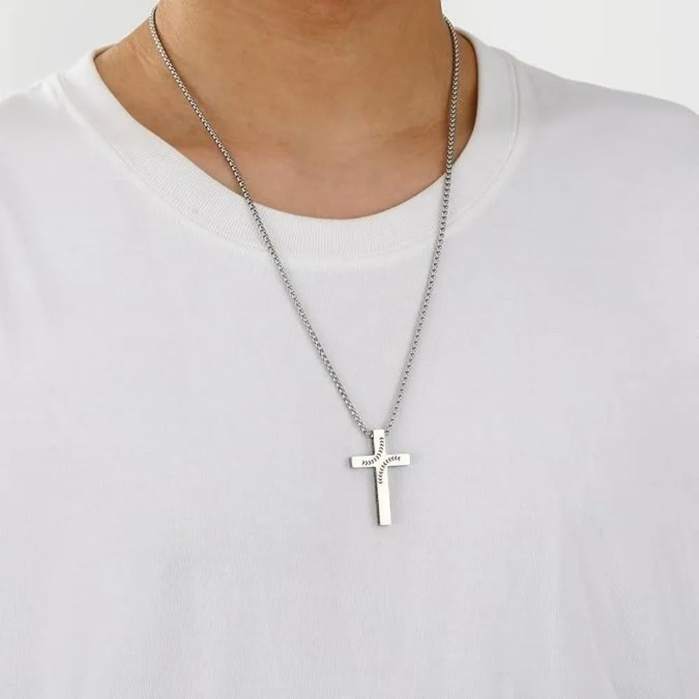A silver stainless steel cross pendant necklace worn around the neck against a white t-shirt.