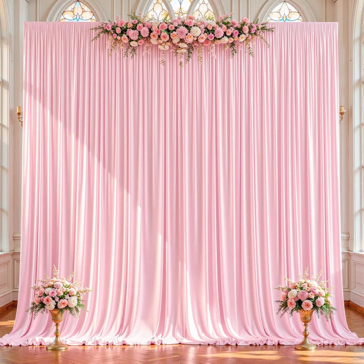 A pink draped fabric backdrop with a floral arrangement across the top, used for an event setting.
