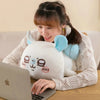 A woman is cuddling a white Chiikawa Hachiware plush pillow with blue ears while using a laptop.