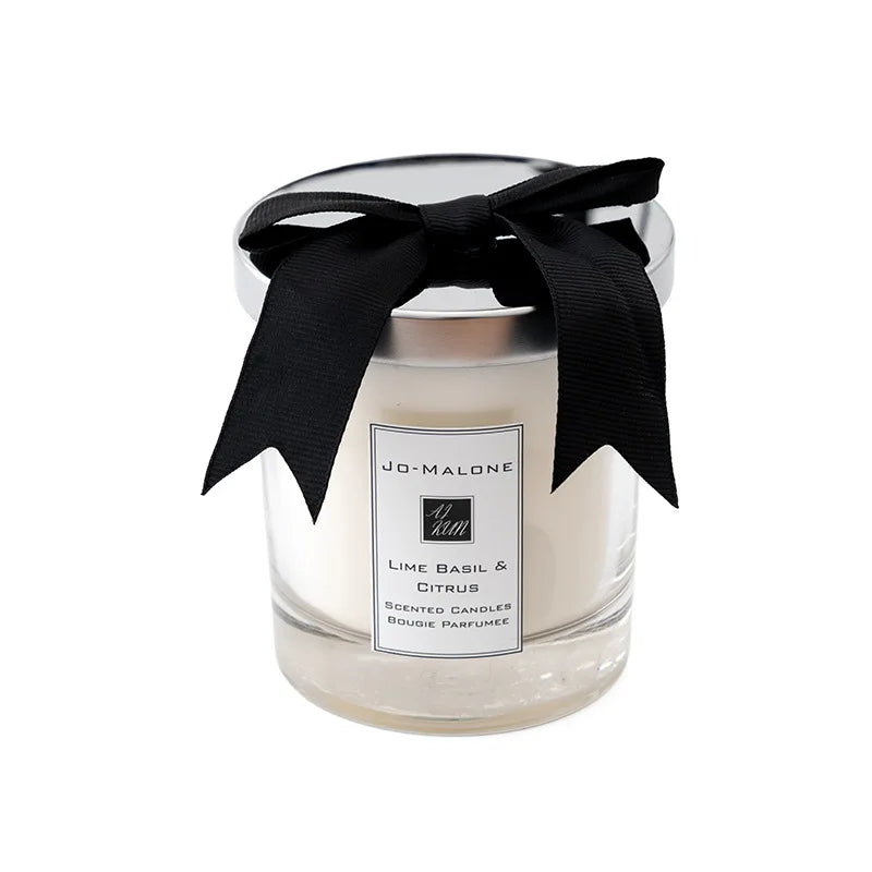 A glass candle cup with a black ribbon tied around the lid, featuring Lime Basil & Citrus scent.