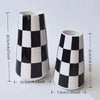A tall ceramic tabletop vase with a black and white checkered pattern.