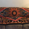 A close-up of a Bohemian mandala tapestry wall hanging featuring orange, yellow, and white patterns on a black background.