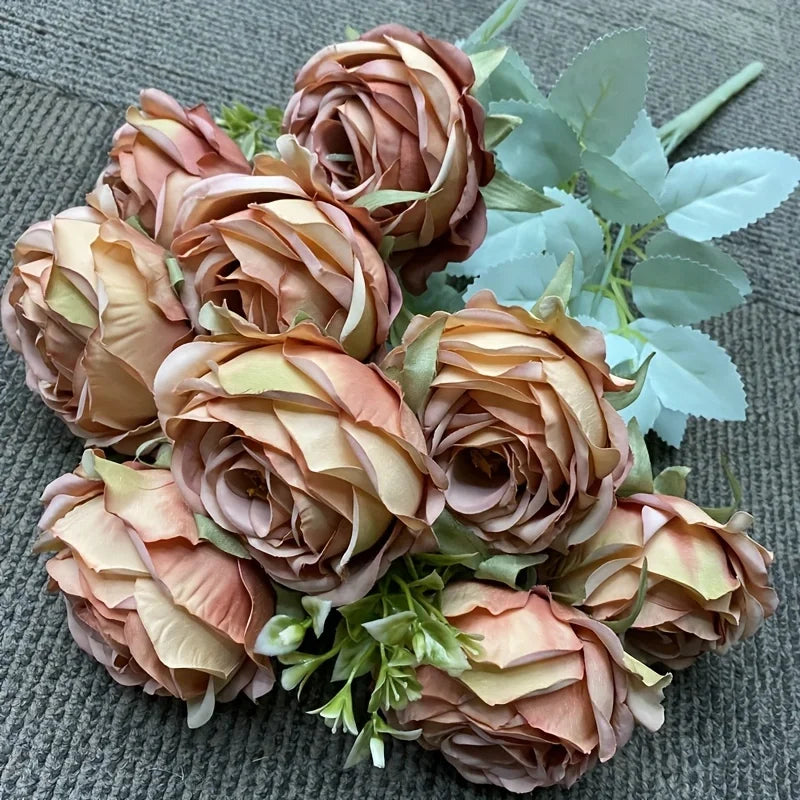 A bouquet of nine silk roses in shades of peach and blush pink with green foliage.