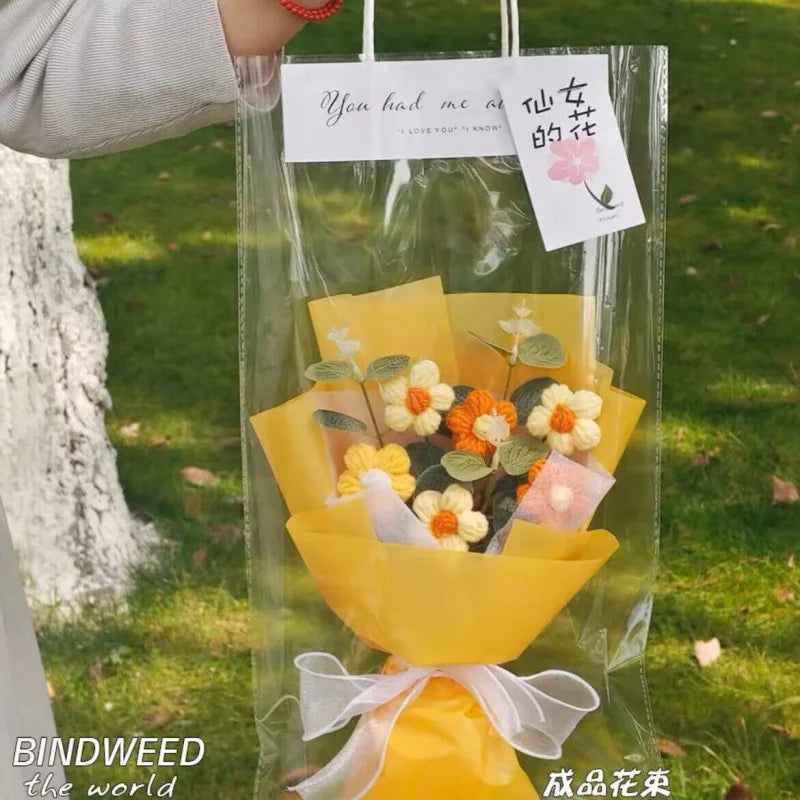 A clear plastic bag containing a yellow handmade crochet flower bouquet with pink and orange accents.