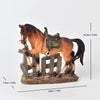 A rustic western horse sculpture with a dark brown coat and green saddle standing on a wooden fence.
