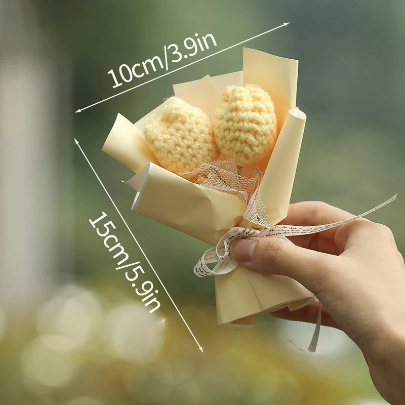 A hand holds a bouquet of handmade yellow crochet flowers wrapped in light beige paper.