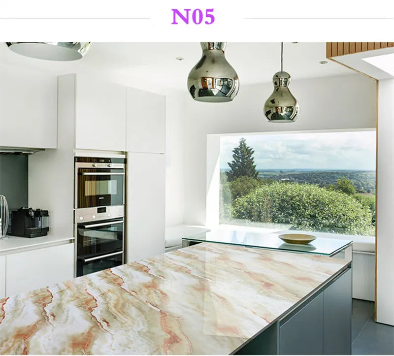 A kitchen countertop made of marble contact paper with pink and beige veining, featuring modern cabinetry and a large window 