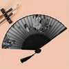A black hand folding fan decorated with gray lines and floral patterns, shown against a light background.
