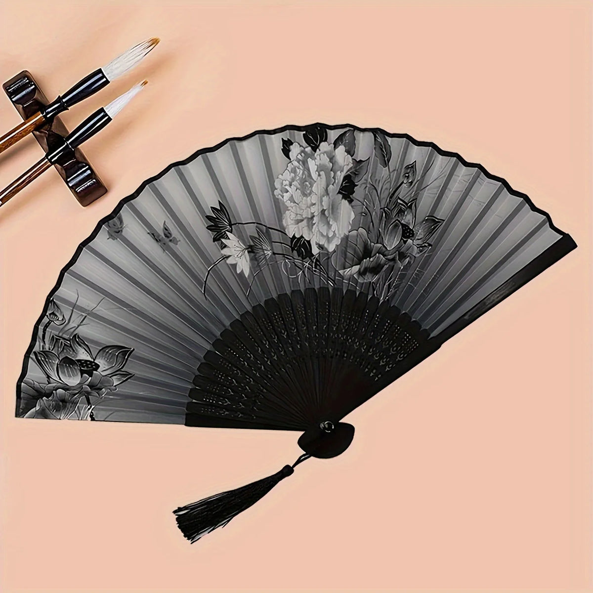 A black hand folding fan decorated with gray lines and floral patterns, shown against a light background.
