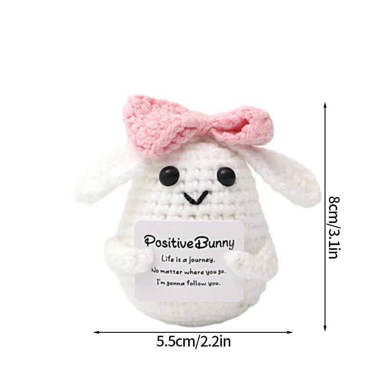 A handmade white crochet bunny doll with pink ears and a slogan stitched on its body.
