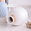 A white ceramic water ripple vase with a natural jute stopper and a blue glass vase in the background.