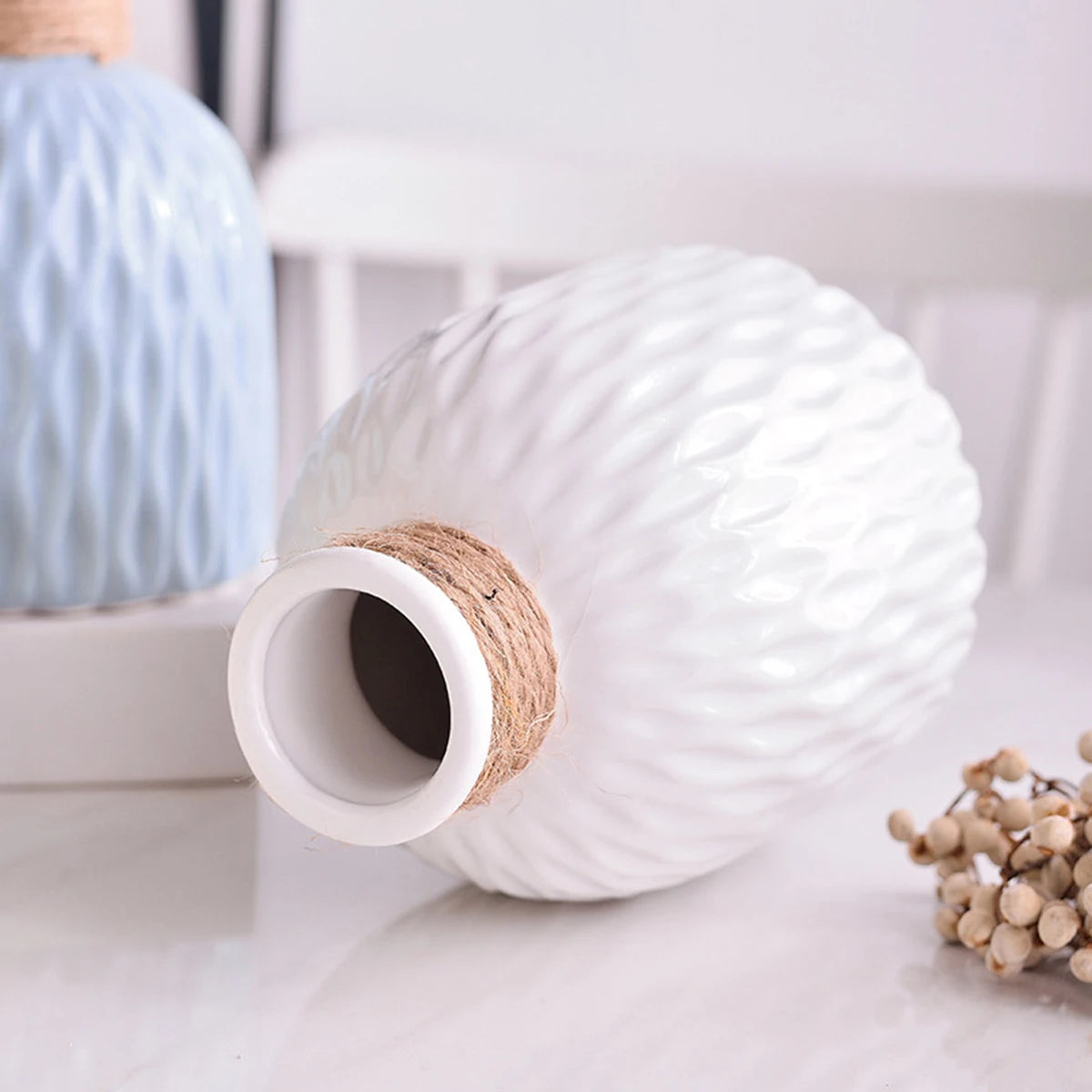 A white ceramic water ripple vase with a natural jute stopper and a blue glass vase in the background.