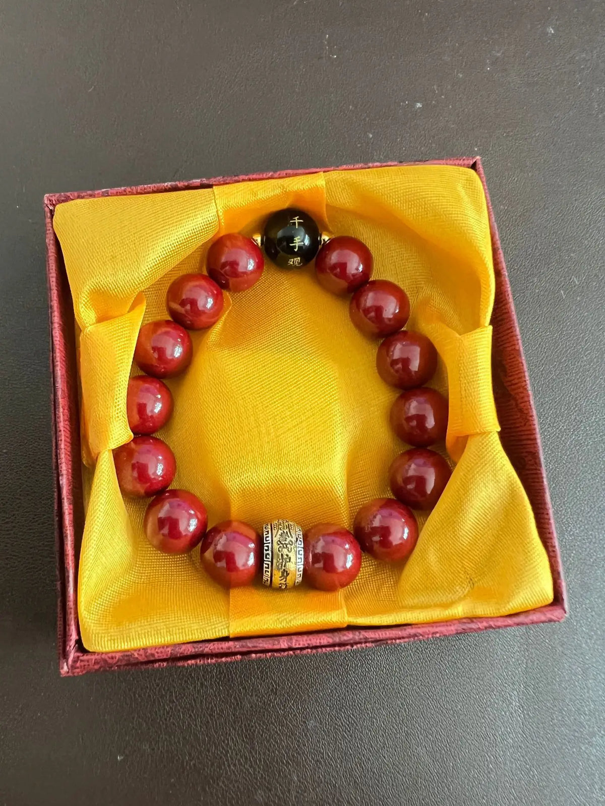 A bracelet of polished red cinnabar stones is displayed in a yellow velvet box.