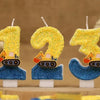 Three yellow construction excavator birthday cake candles with glittery numbers 1, 2, and 3