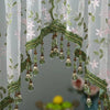 A lace door curtain featuring green foliage and pink flowers with hanging beads.