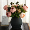 A bouquet of pink and peach peony artificial flowers in a dark vase with a photo frame.