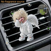 A cute white acrylic teddy bear with gold accents is clipped onto a car vent for decoration.