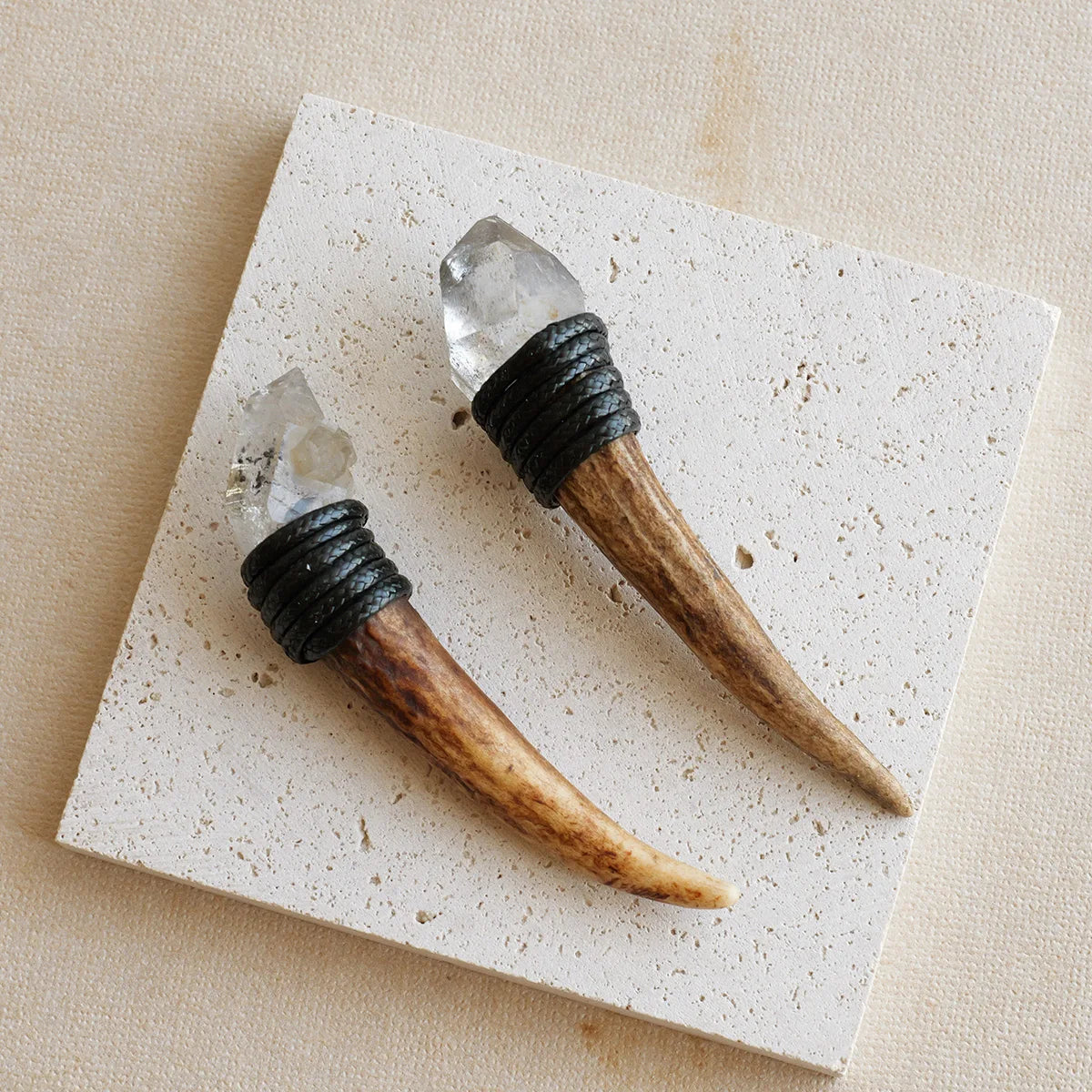 A natural crystal Herkimer scepter wand with a dark handle rests on a white square tile.