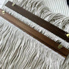 A dark brown wooden dowel with brass hardware is laid diagonally across a light beige macrame textile.