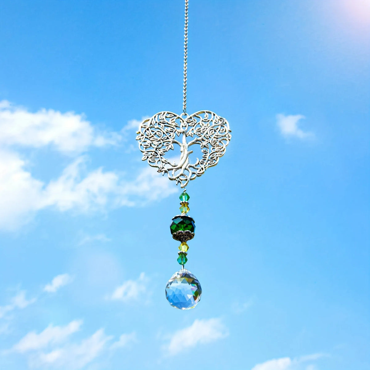 Silver crystal tree of life pendant with colorful gemstone drops suspended against a bright blue sky