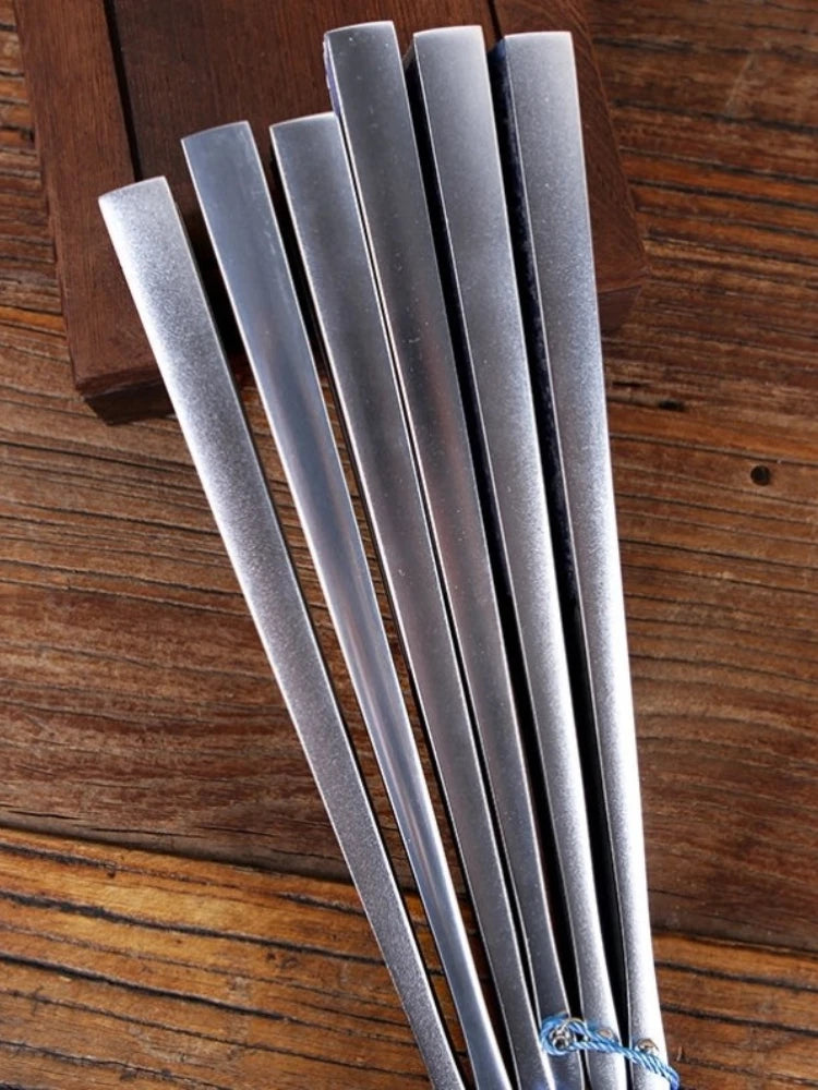A set of five silver titanium alloy folding hand fans arranged diagonally on a wooden surface.