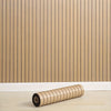 Roll of self-adhesive 3D wood grain wall panels lying on a light wooden floor.