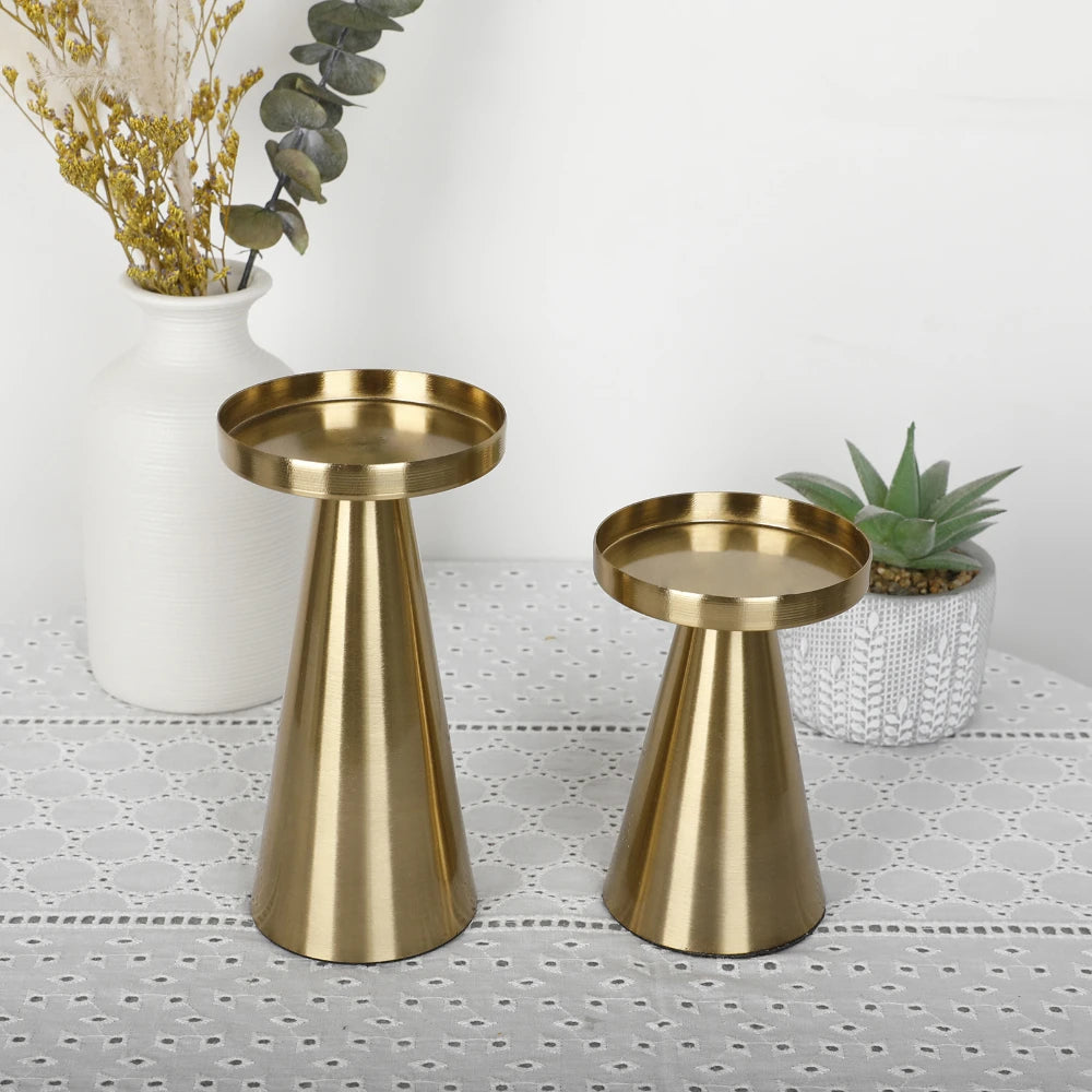 A set of three elegant gold metal candle holders displayed on a white surface with dried flowers and greenery.