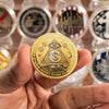 A hand holds a golden commemorative coin featuring an eye design and the text Money Flows to Me.